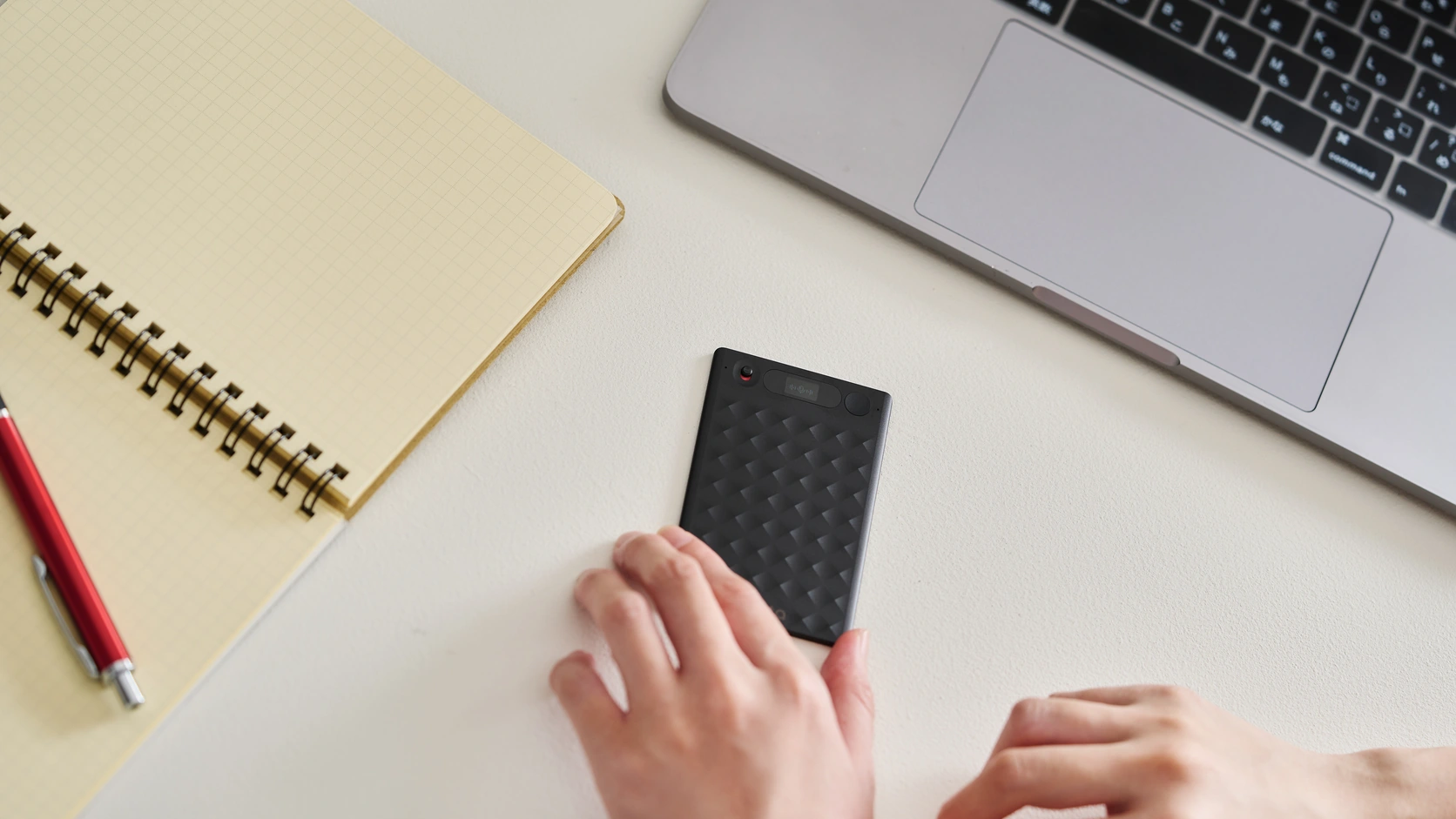 Notta Memo recorder beside a notebook and laptop, with a hand holding the device