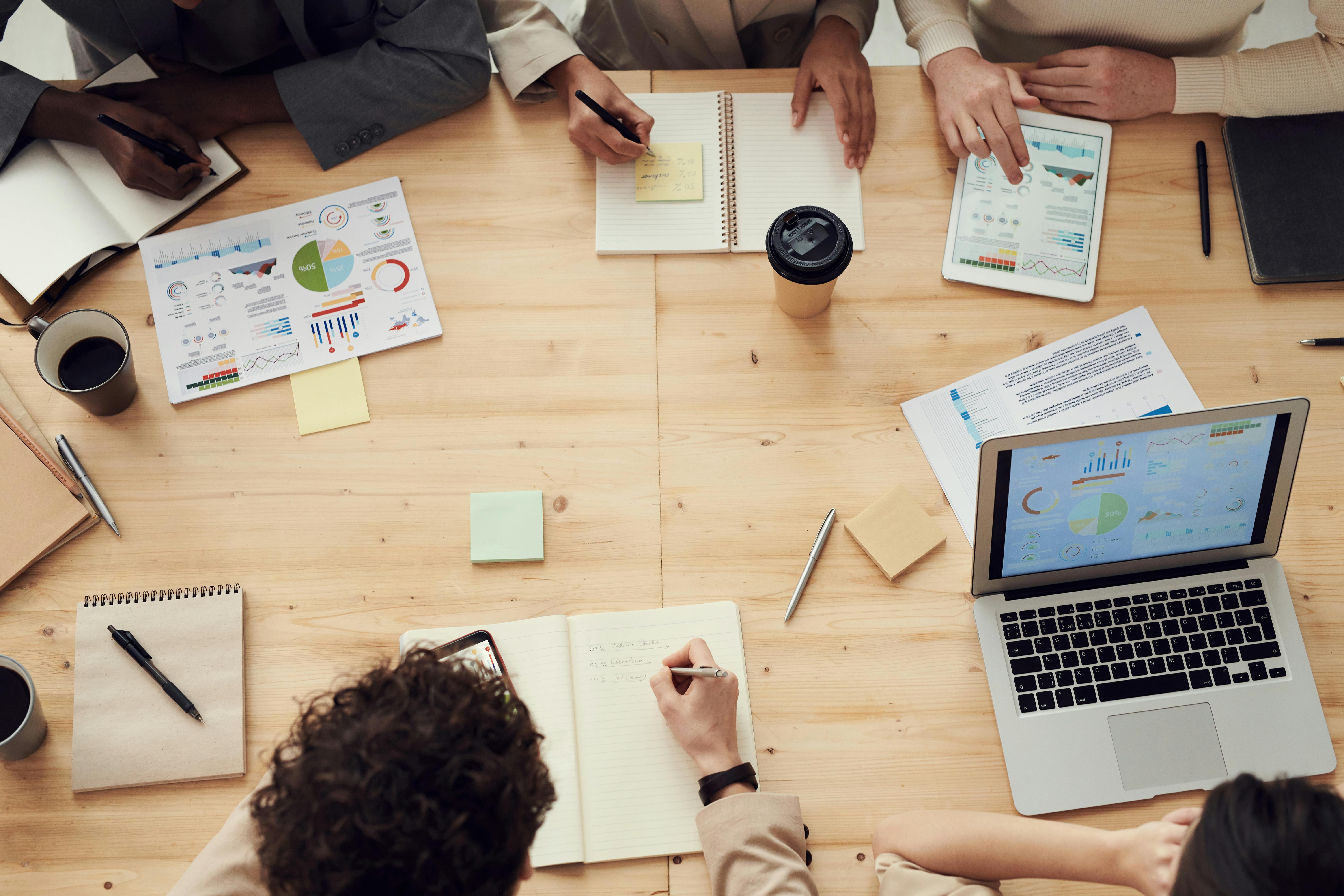 Professional meeting room with people taking notes during a business meeting, showing templates and documentation on laptops and notebooks