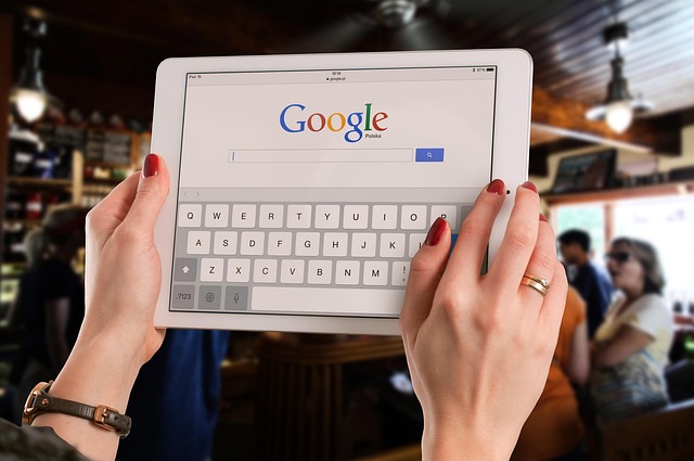 Google検索ページを表示したタブレットを両手で持つ人。ネパール語翻訳に強いアプリやツールを調べている様子を表し、ネット検索で情報収集するイメージ。