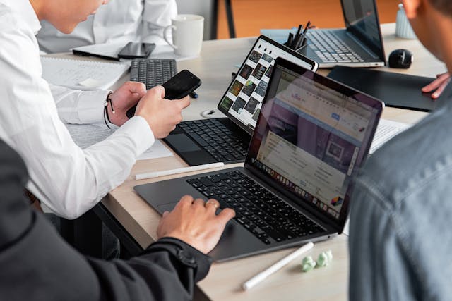 ノートパソコンやスマートフォンを使って資料を確認しながら打ち合わせを行うビジネスチームの様子