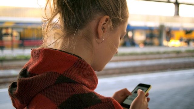 駅で電車を待ちながらスマホで情報をチェックする女性。ドイツ語翻訳アプリを使って現地の案内や列車情報を確認するイメージ。