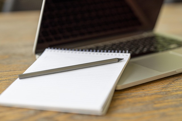 ノートパソコンのキーボードにリングノートと鉛筆を置いたイメージ。ペーパーレス会議でも必要な端末とメモ用具を整えている様子で、紙資料からデジタル資料へ移行するメリットを強調。