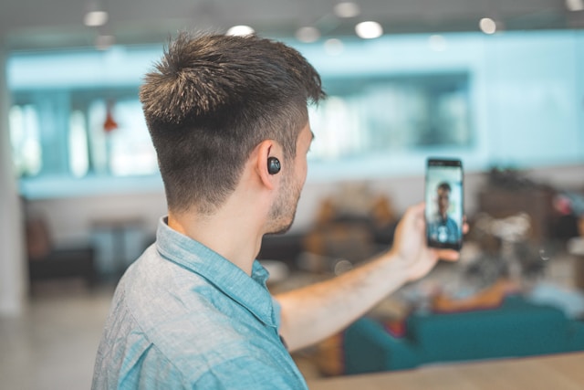 ワイヤレスイヤホンを装着してスマートフォンでビデオ通話する男性の後ろ姿。海外との通話やオンライン会議で音声翻訳アプリを利用する場面を想起させる。