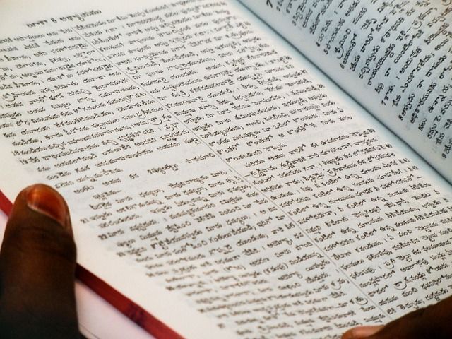 手元の本にタイ文字がびっしりと書かれている。翻訳アプリを使ってタイ語の書籍や資料を読み解き、学習を進めるシーンを示している。