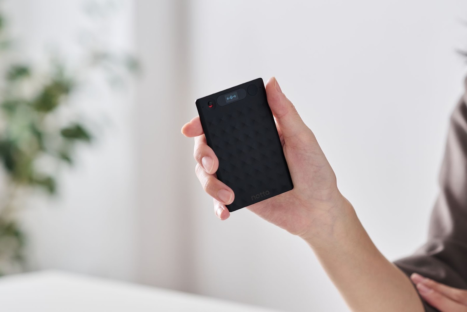 女性が外部録音デバイス「Notta Memo」を持っている。洗練されたデザインで、片手に収まるコンパクトなサイズ。