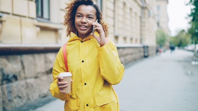 コーヒーを手に通話している女性。日常生活や留学先で、ドイツ語翻訳ツールを活用して現地の人と会話するシーンにぴったり。