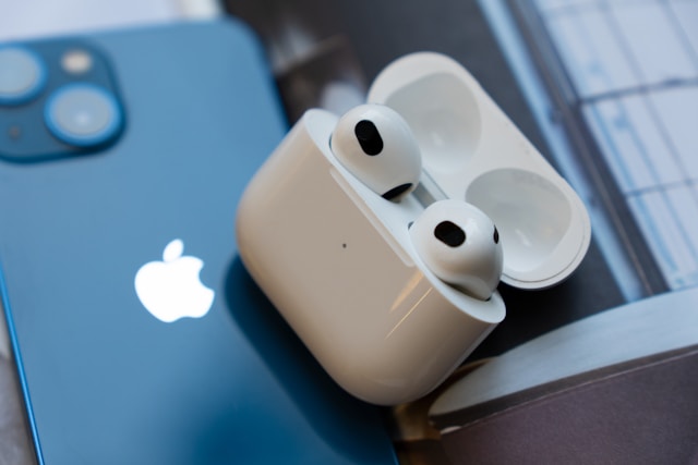 ブルーのiPhoneの上に置かれたAirPods 第3世代のイヤホンと充電ケース。iPhoneとの相性の良さがわかる一枚