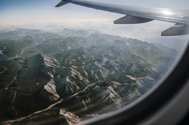 飛行機の窓から見える雄大な山脈と機体の翼を撮影した写真。海外旅行へ向かう機内で翻訳アプリを使うシーンを連想させます。