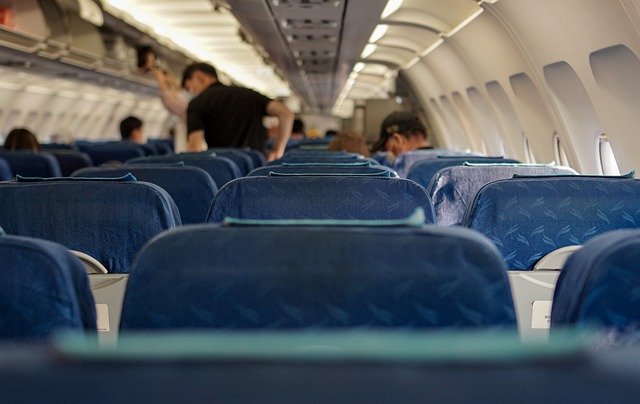 青いシートが並ぶ飛行機の客室内と乗客の姿を捉えた写真。海外旅行中に翻訳アプリが役立つシーンを示しています。