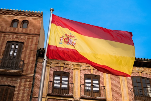 歴史的な建物の前に掲げられたスペイン国旗。スペイン語翻訳アプリやサービスの特集記事の背景に適したイメージです。