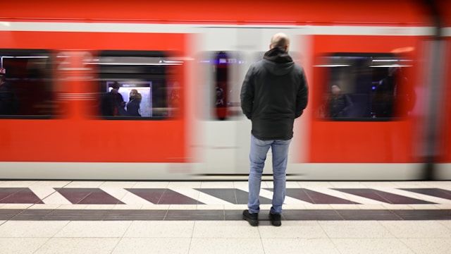 ドイツの公共交通機関の駅で、電車を待つ人の後ろ姿。旅先で交通案内を翻訳アプリで調べる際の雰囲気を伝える。