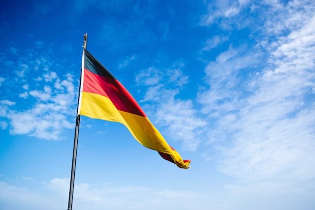 澄んだ空の下で翻るドイツ国旗。ドイツ語翻訳や旅行関連の記事の導入として、国の象徴と翻訳の重要性を示す。
