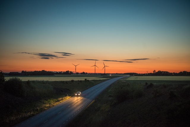 日没前の田園風景に風力発電のタービンが並び、一本の道路を車が走っている。自然あふれる旅行でも翻訳アプリが役立つことを示すイメージ。