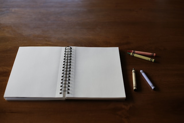 白紙のスパイラルノートと色鉛筆。大学ノートの色分けルールや記号・下線の使い分けで視認性を高めるイメージ。