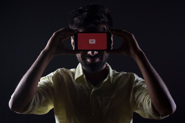 YouTubeアプリを表示したスマホを掲げる男性｜YouTube動画を高画質で保存・オフライン視聴する方法のイメージ